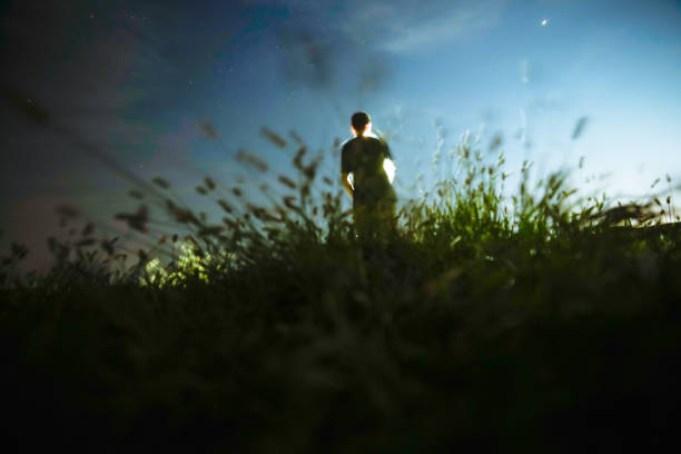 istock one man standing in the grass field under sky at night 1033048542