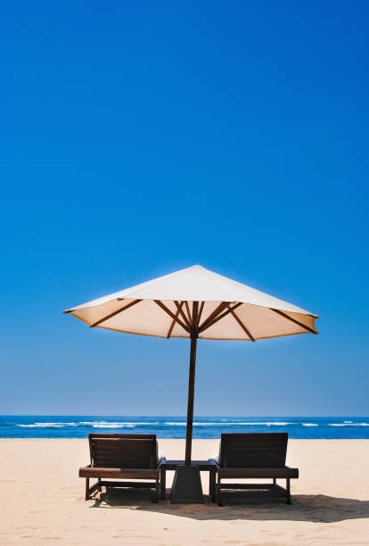 zwei liegestühle unter einem regenschirm, stehend in den sand am strand von nusa duo. - coastline noosa heads australia landscape stock-fotos und bilder