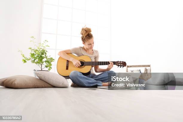 Photo libre de droit de Jouer De La Guitare Belle Jeune Femme Avec Ordinateur Apprendre À Jouer Avec Un Cours En Ligne Assis Sur Le Sol Dans Des Vêtements Décontractés À La Maison banque d'images et plus d'images libres de droit de Guitare