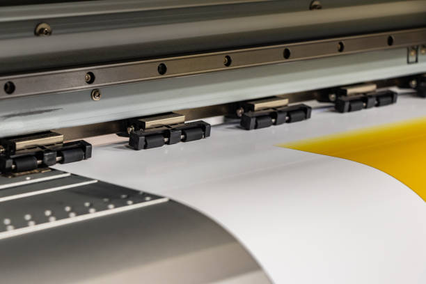 istock Big professional printer, processing a massive roll of glossy paper for a large scale billboard project. Deep saturated yellow ink and motion blur from the printing head. 1033149588