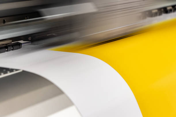 istock Big professional printer, processing a massive roll of glossy paper for a large scale billboard project. Deep saturated yellow ink and motion blur from the printing head. 1033149678
