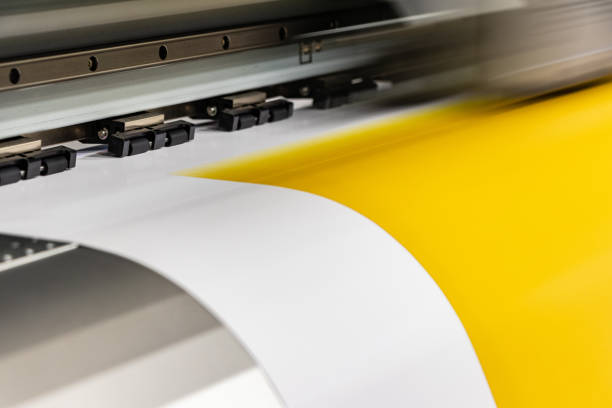 istock Big professional printer, processing a massive roll of glossy paper for a large scale billboard project. Deep saturated yellow ink and motion blur from the printing head. 1033149686