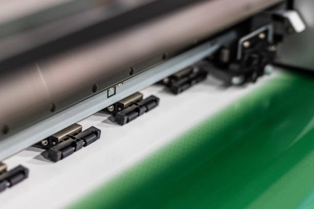 Detailed shot of a print head passing by while processing a large, glossy, green, roll of premium paper.