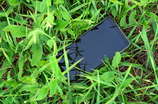 the lost mobile phone is on the ground among the green grass in the open air