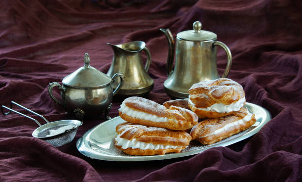 istock eclairs, choux pastries filled with whipped cream, dark violet background, silver dinnerware 1033237214