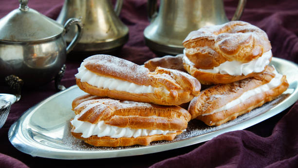 istock eclairs, choux pastries filled with whipped cream, dark violet background, silver dinnerware 1033240664