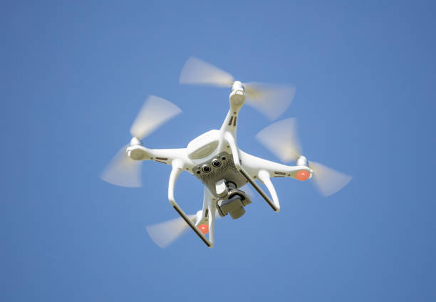 White drone with digital camera, filming from above. Proper for aerial surveillance. Clear blue sky background.