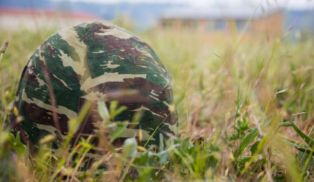 Military camouflage helmet putted down on the ground. Anti-war symbol. Soldier got tired of war. Close up front view, blurred nature background, space for text.