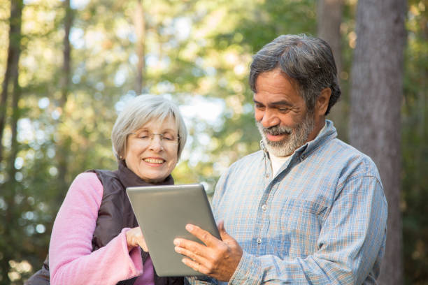 アクティブ シニアの大人のカップルは屋外デジタル タブレットを使用します。 - autumn senior adult mature couple active seniors ストックフォトと画像