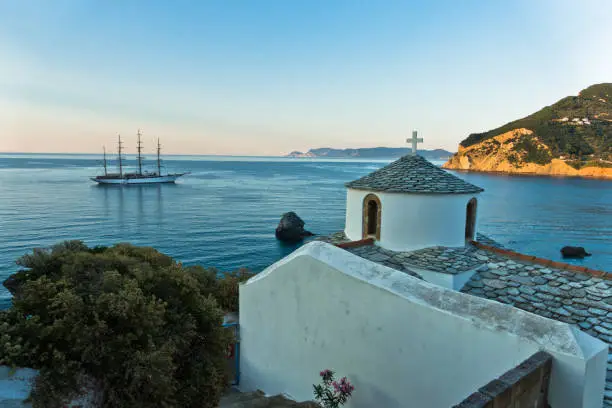 Small church and sailing ship at sunset in front of city harbor, Skopelos island in Greece