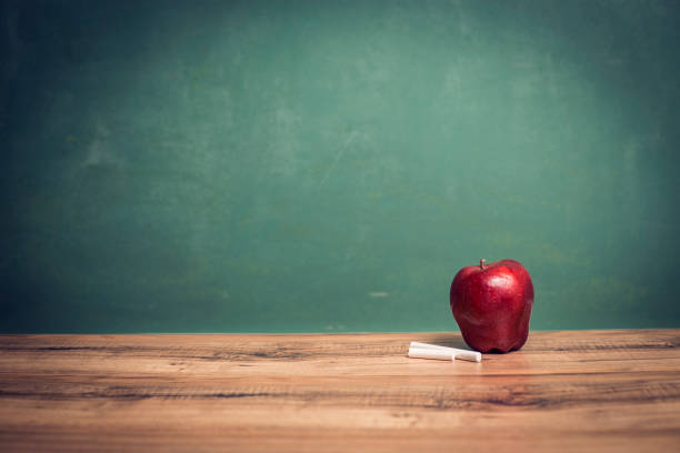 istock Apple, chalk on wooden school desk with chalkboard. 1033277952