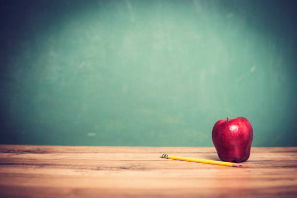 istock Apple, pencil on wooden school desk with chalkboard. 1033278040