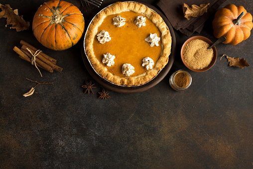 Pumpkin Pie with whipped cream and cinnamon on rustic background, top view. Homemade pastry for Thanksgiving traditional Pumpkin Pie.