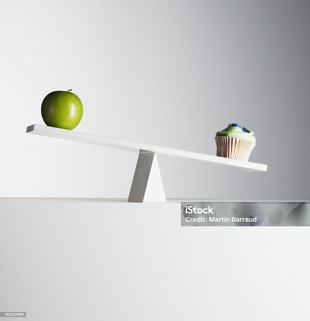 Cupcake tipping seesaw with green apple on opposite end  Weight Scale Stock Photo