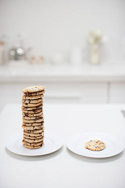 Stack of cookies on plate next to single cookie on plate  unfairness stock pictures, royalty-free photos & images