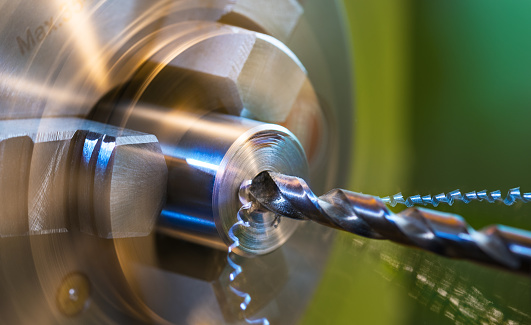 Close-up of a metallic workpiece clamped in a rotating machine chuck. Steel drill bit and twisted swarfes on a green background. Cutter, axial hole, metal chips. Machining. Beautiful motion blur