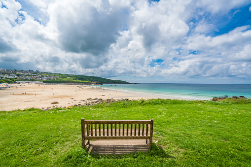 St. Ives, England -  June 2018 : Empty wooden bench for tired walkers on the coastal path along the Cornish coast with a view of Porthmeor beach, Cornwall