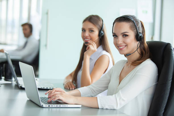 istock Beautiful business people in headsets are using computers and smiling while working in office. Girl is looking at camera. 1033382000