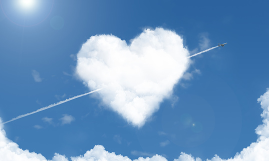 A heart shaped cloud and flying airplane in the blue sky