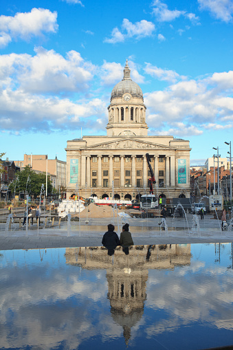 Two african ethnicity girls met at the Old Market square in Nottingham to discuss thing in person. A perfect reflexion of The Exchange building in the pond.