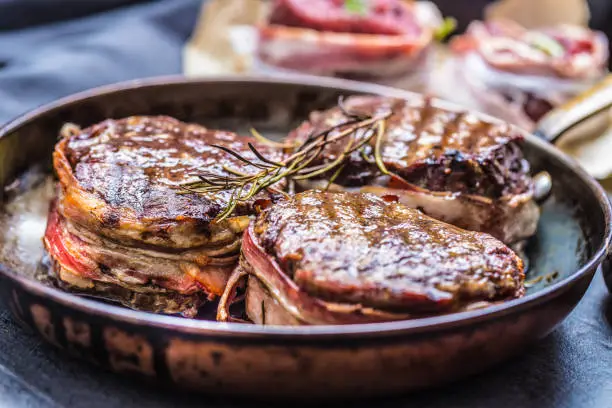 Photo of Three grilled beef tenderloin steaks coated bacon on a frying pan.