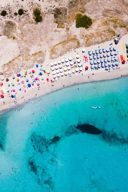Photo of Aerial view of an emerald and transparent Mediterranean sea with a white beach full of beach umbrellas and tourists who relax and take a bath. Gulf of the Great Pevero, Costa Smeralda, Sardinia, Italy.