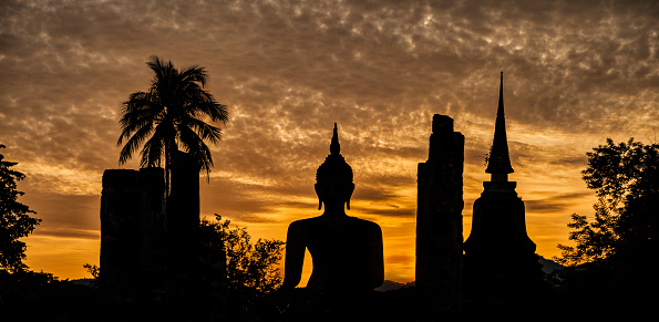 Silhouette of a Buddha statue and a temple at sunset in Thailand.