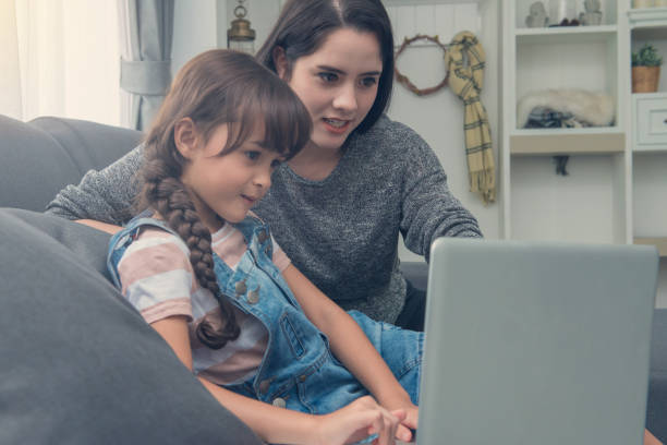 istock Beautiful young mom and daughter are using notebook on sofa at home 1033519918