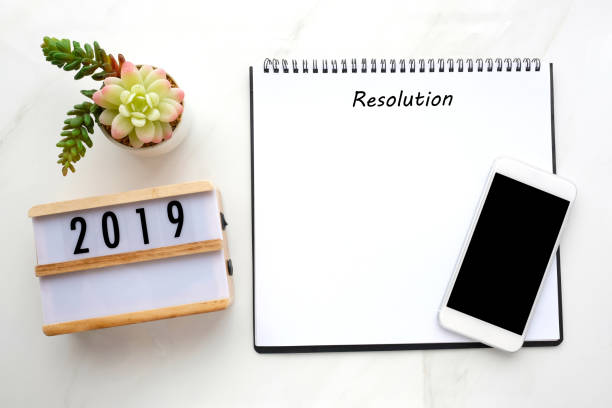 istock 2019 resolution on blank notebook paper, smart phone with blank screen on white marble background, 2019 new year mock up, template, flat lay 1033552778