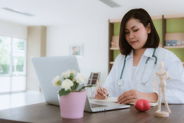 istock Portrait of female doctor is taking note while looking at laptop computer 1033564546