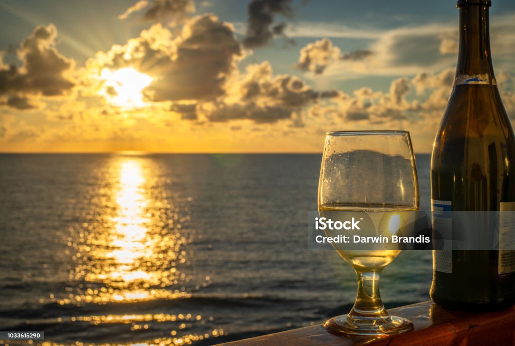 Wine on the Water A generous pour of of Champagne paired with a brilliant waterfront sunset/sunrise. Chablis Wine Stock Photo