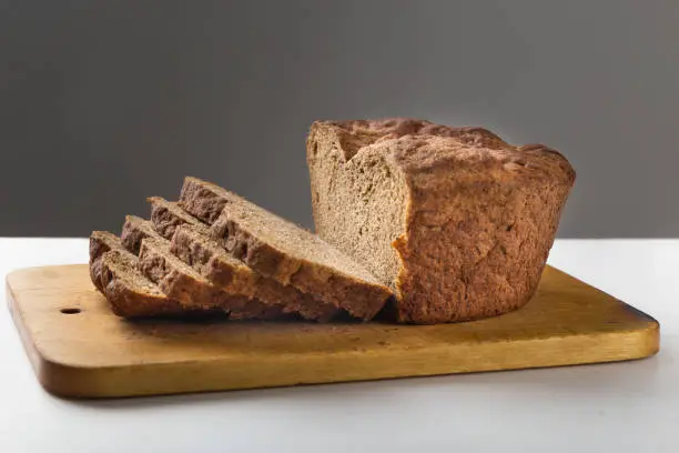 Rye bread, on a wooden board is cut with segments, gray background. Copy space