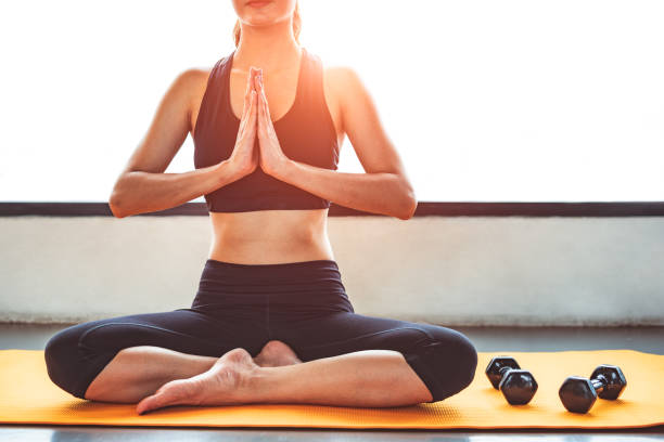 Front view beauty woman doing yoga and raise hand or pay obeisance in fitness workouts training gym center. Lifestyle sport woman sitting on mat with sport equipment and exercise dumbbells background frente mujer de belleza vista haciendo yoga y levanta la mano o pagar reverencia en los entrenamientos de fitness gimnasio centro de entrenamiento. mujer de deporte estilo de vida sentado en la estera con el fondo de deporte equipos y ejercicio pesas