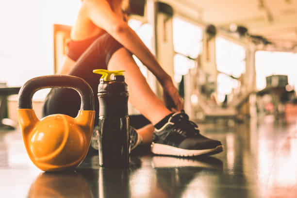 cerca kettlebells con rutina de ejercicio de mujer en la última hora de fitness gimnasio relajarse después de un entrenamiento de deporte con fondo de botella de batido de proteína. atleta y estilo de vida saludable culturismo músculos mancuernas. - gimnasio escolar fotografías e imágenes de stock