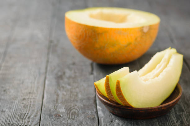 istock Ripe melon pieces on a clay bowl and half a melon on a wooden table. 1033633862