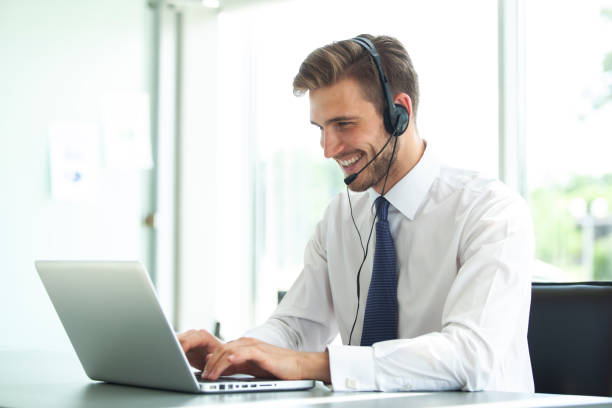 szczęśliwy młody mężczyzna obsługi klienta wykonawczego pracy w biurze. - receptionist desk computer laptop zdjęcia i obrazy z banku zdjęć