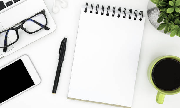 istock Blank notebook page in the middle of white office desk table. Top view, flat lay. 1033662530