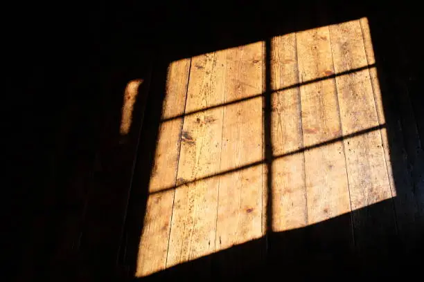 Hampshire, England - September 2, 2018: the bright afternoon sun falls from a window onto old timber floorboards, casting shadows of the window's frame.