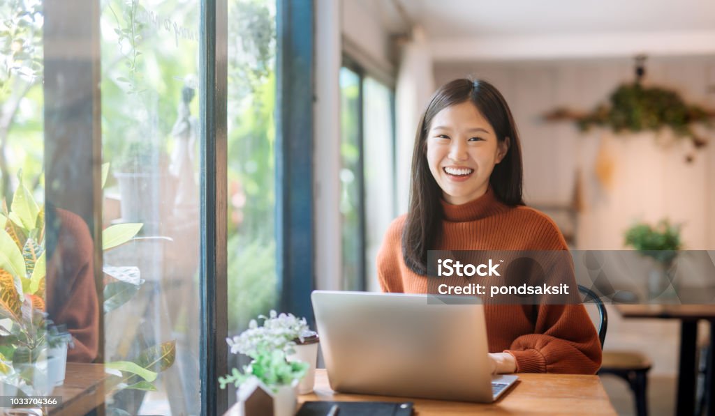 young Asian girl working at a coffee shop with a laptop Happy young Asian girl working at a coffee shop with a laptop Women Stock Photo