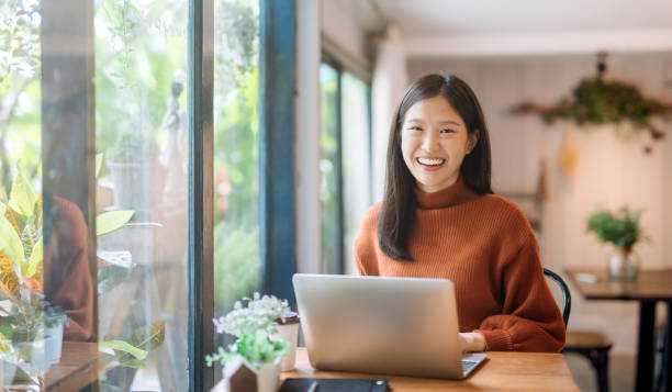 young Asian girl working at a coffee shop with a laptop Happy young Asian girl working at a coffee shop with a laptop korean ethnicity photos stock pictures, royalty-free photos & images