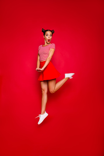 Full-length full-size vertical view of jumping and wondered brunette woman dressed in colourful bright clothes isolated on red background