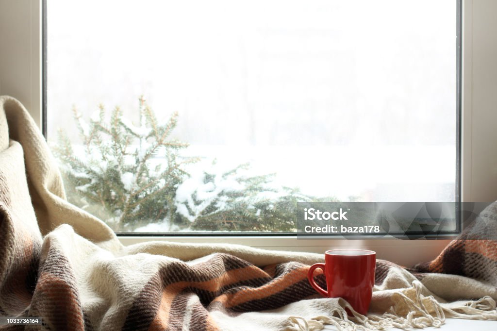 cozy home atmosphere in the winter red mug of hot drink on a windowsill with a warm blanket, when behind is window is snow Winter Stock Photo