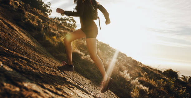woman running up a rocky mountain slope - colina acima imagens e fotografias de stock