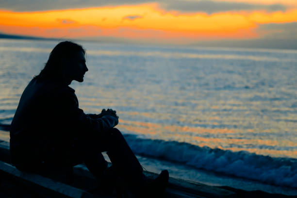 istock guy standing by the sea at sunset 1033750980