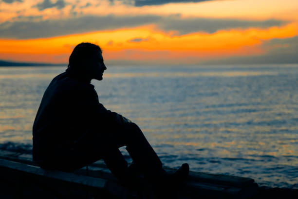 istock guy standing by the sea at sunset 1033750982