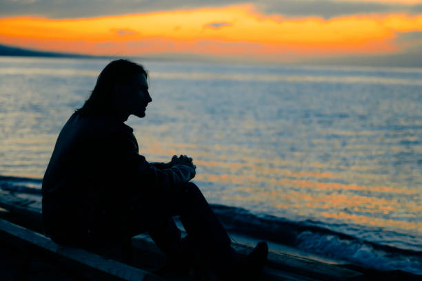istock guy standing by the sea at sunset 1033750984