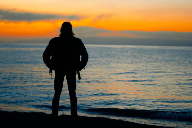 istock guy standing by the sea at sunset 1033750996