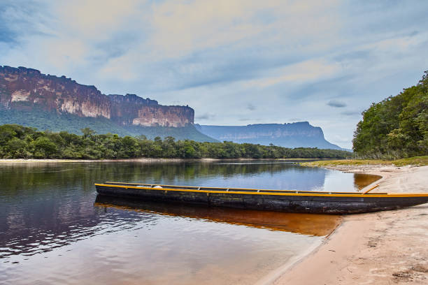 Excursion boat to the river bank in Canaima Canoe in river, with mountain and cloudy sky in the background guyana stock pictures, royalty-free photos & images