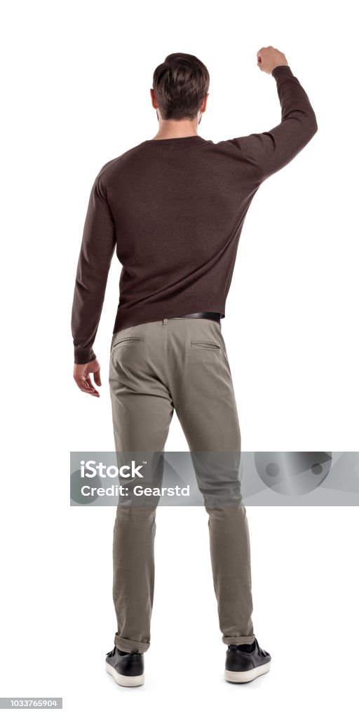 A fit man in casual sweater stands in a back view with one arm lifted up as if holding something in front of him. A fit man in casual sweater stands in a back view with one arm lifted up as if holding something in front of him. Careful hold. Showing something in hand. Back view on man. Rear View Stock Photo