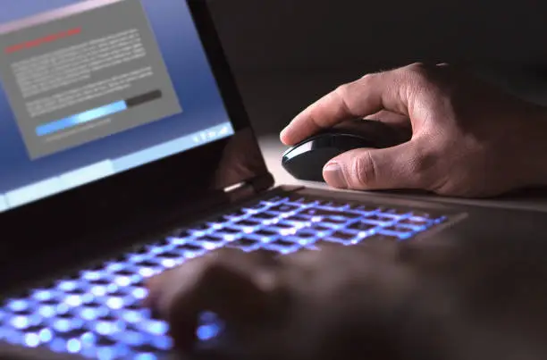 Photo of Man installing software in laptop in dark at night. Hacker loading illegal program or guy downloading files.